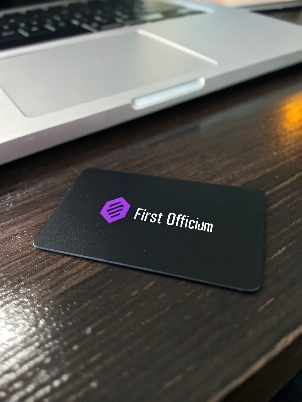 A professional business card with the First Officium logo and contact details, placed on a modern desk with a laptop in the background, symbolizing a virtual office setup.